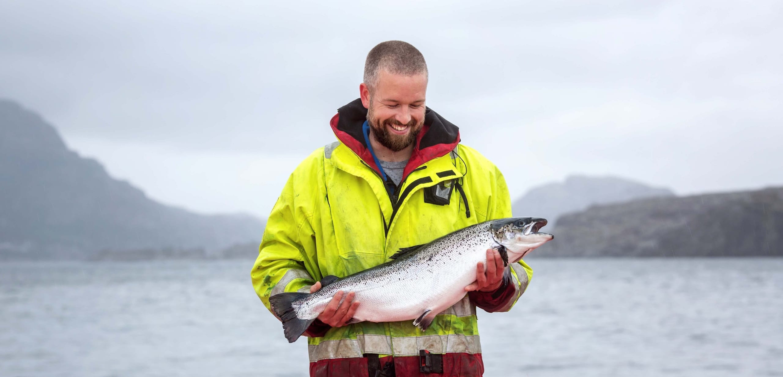 A Norwell farmer holding a freshly harvested salmon by the fjord